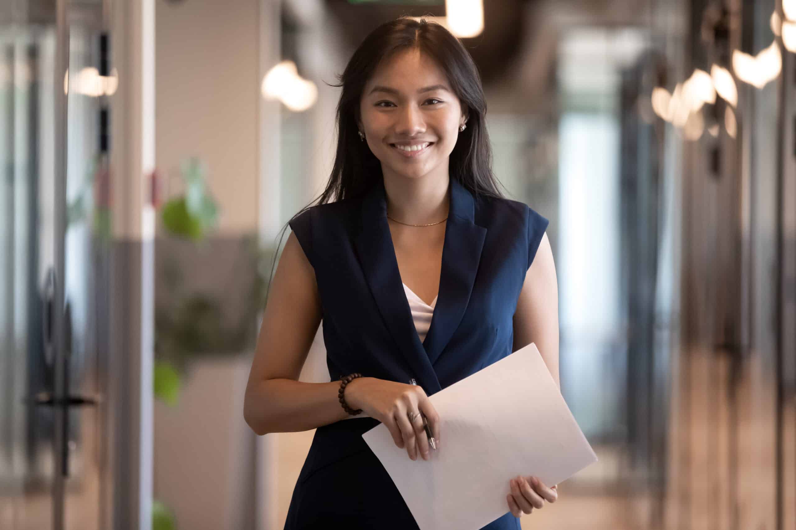Happy,Smiling,Asian,Businesswoman,Looking,At,Camera,Holding,Papers,Stand