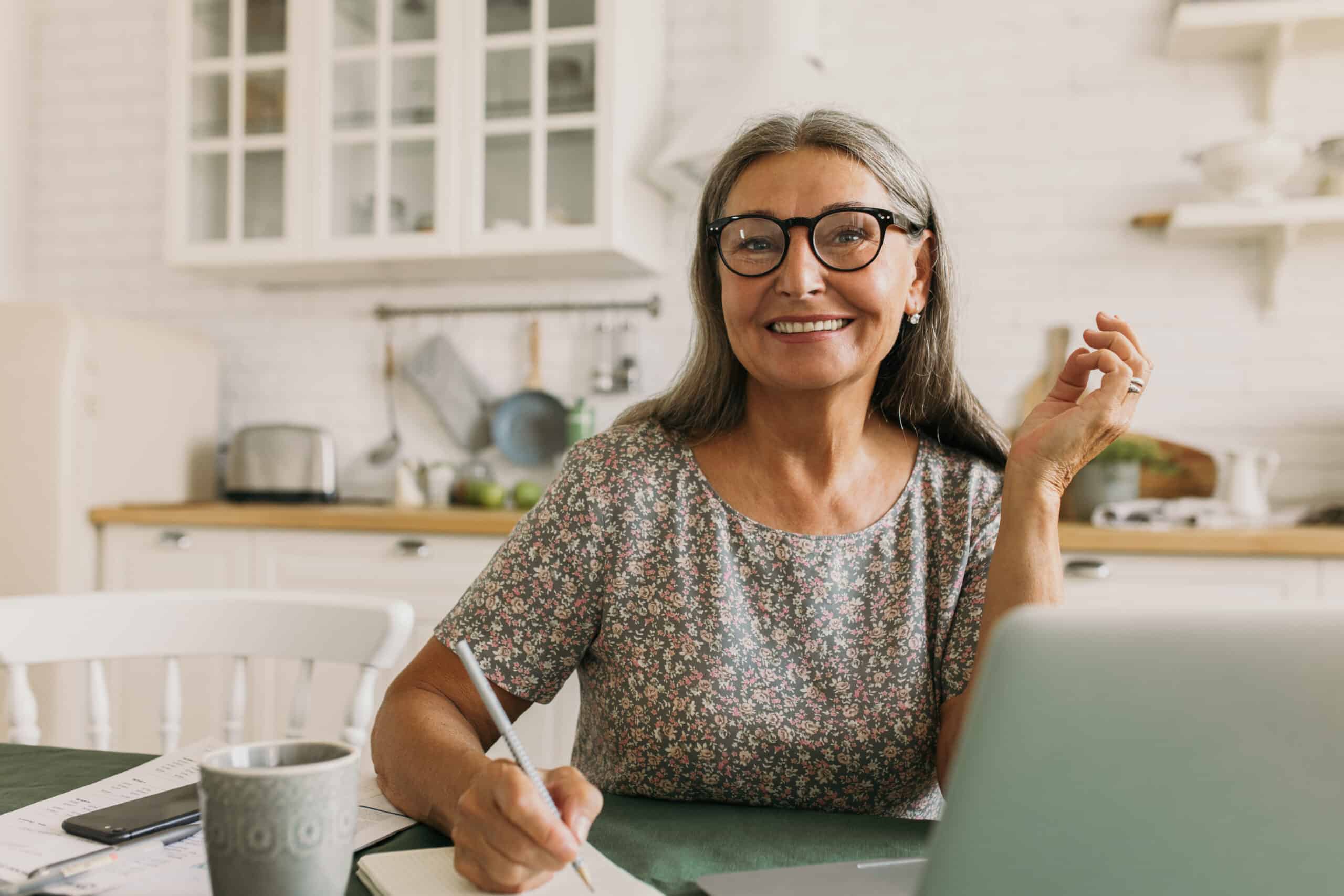 Cheerful,Smiling,Senior,Woman,Making,Notes,In,Diary,,Using,Laptop